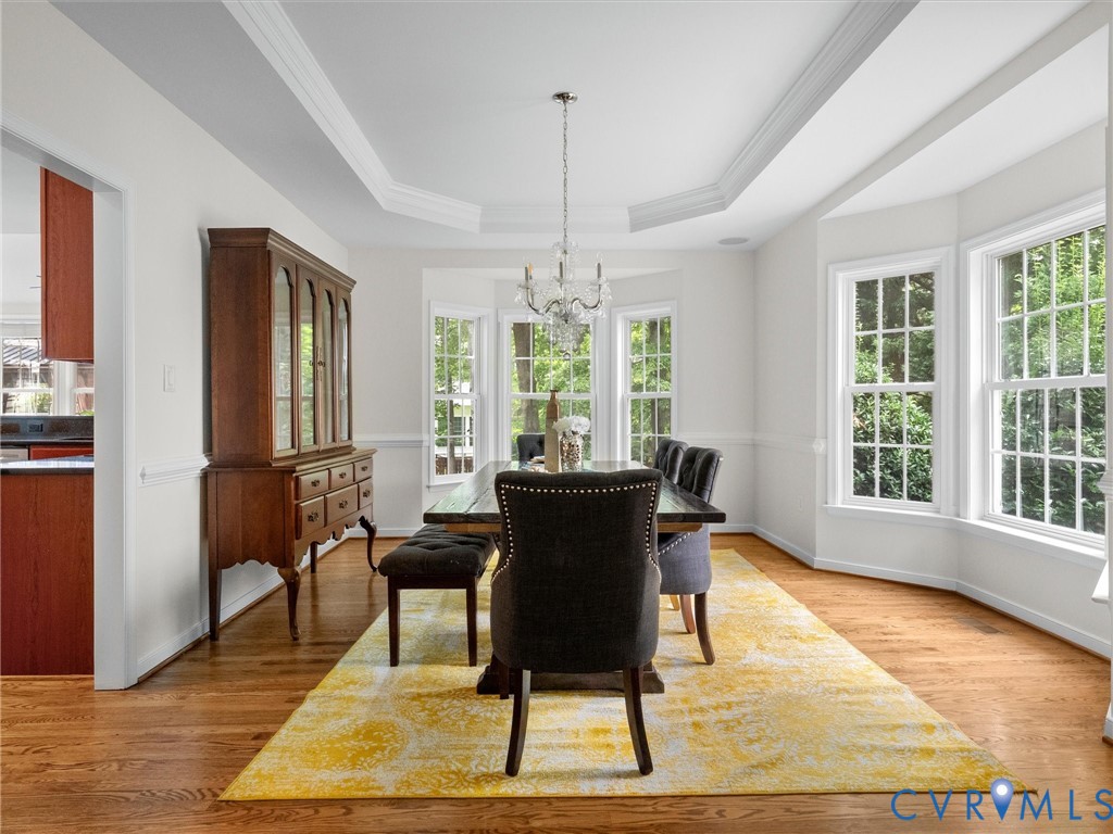 Tray ceiling with crown molding, wood-finish flooring, bay window, chandelier, and chair rail molding