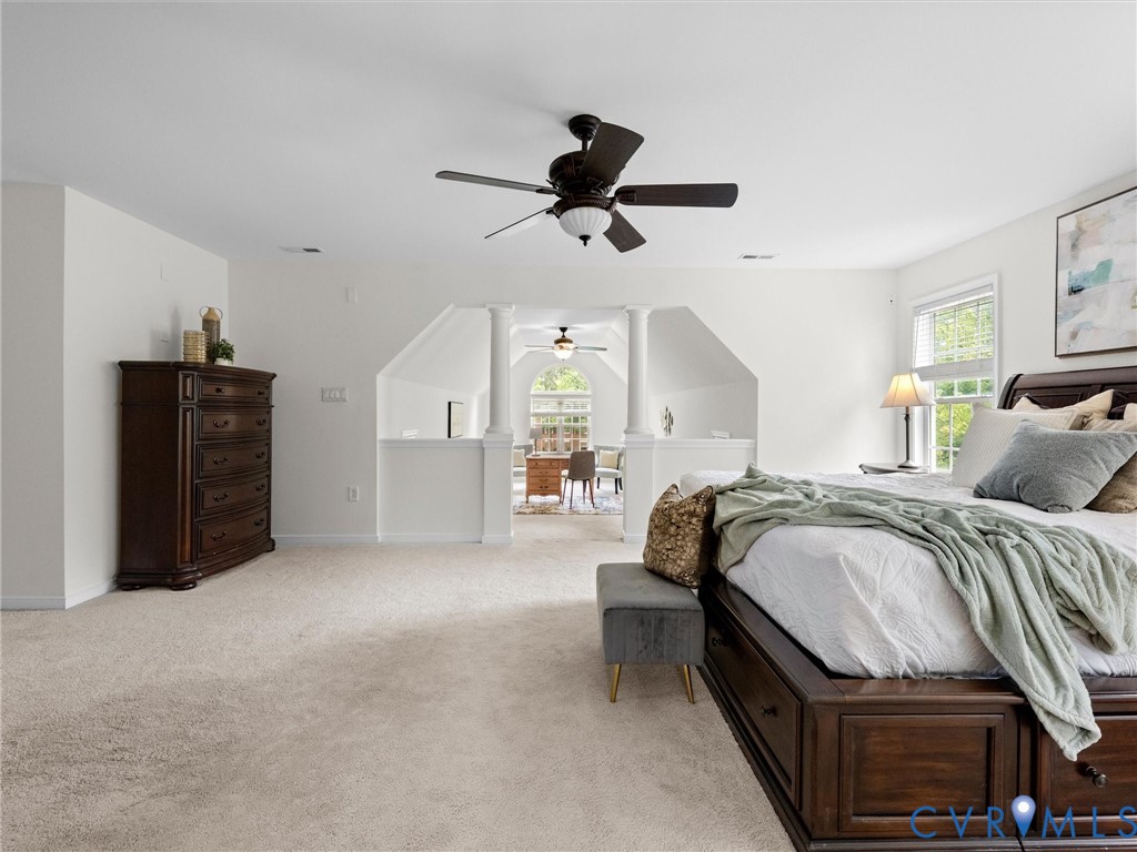 Expansive carpeted room featuring a ceiling fan, window with natural light, and an architectural half-wall design