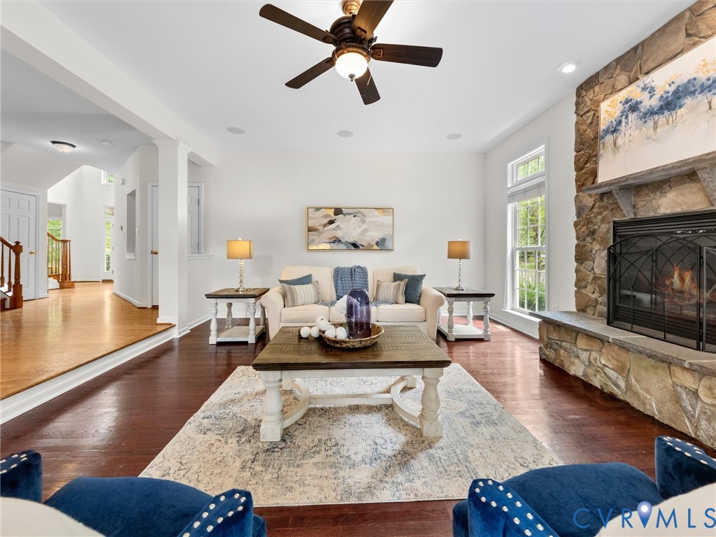 Stone-clad fireplace with hearth, rich wood-finish flooring, recessed lighting, and a ceiling fan
