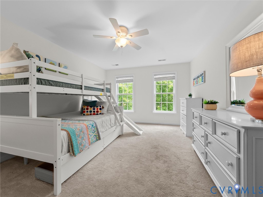 Carpeted flooring, white walls, two windows with blinds, and a ceiling fan with integrated lighting