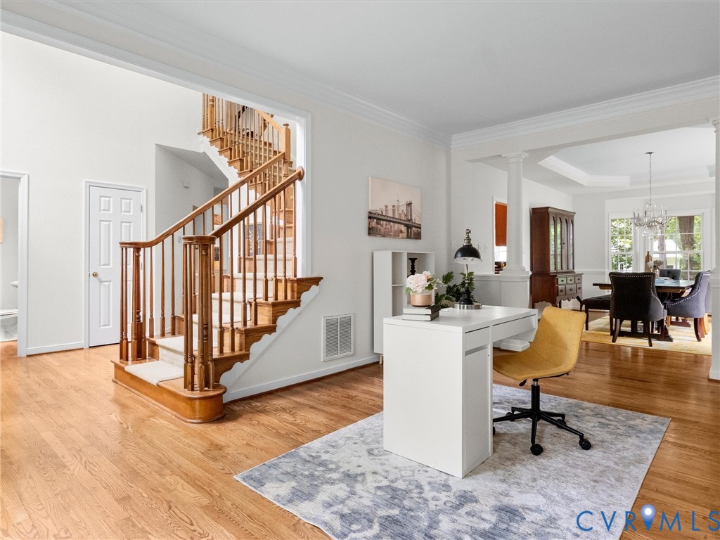 Hardwood flooring, classic wooden staircase with carpeted treads, crown molding, arched entryways, and a tray ceiling