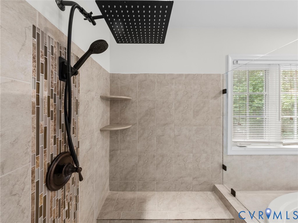 Walk-in shower featuring a rainfall showerhead, handheld shower fixture, and tiled walls with decorative mosaic accents