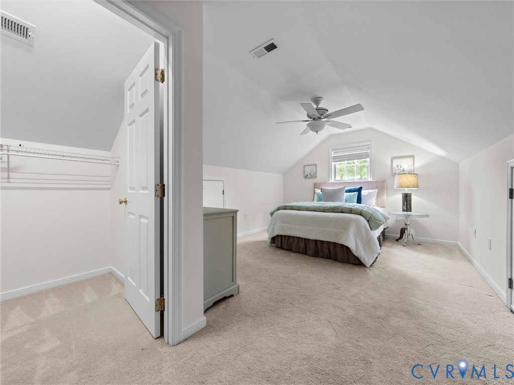 Sloped ceiling bedroom with carpet flooring, a ceiling fan, and a window providing natural light