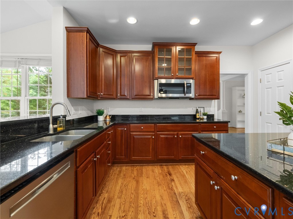 Kitchen featuring wood-finish flooring, dark stone countertops, wood cabinetry, stainless steel appliances, and a vaulted ceiling