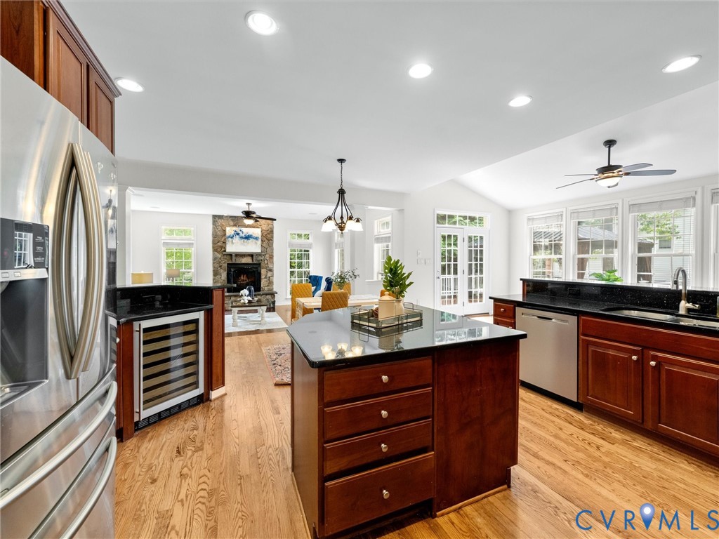 Expansive kitchen featuring wood-finish flooring, stainless steel appliances, dark cabinetry, and black countertops