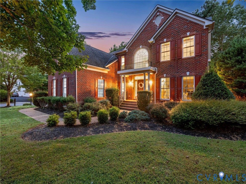 Brick exterior featuring red shutters, a decorative arched window, a covered portico, and a second-story balcony