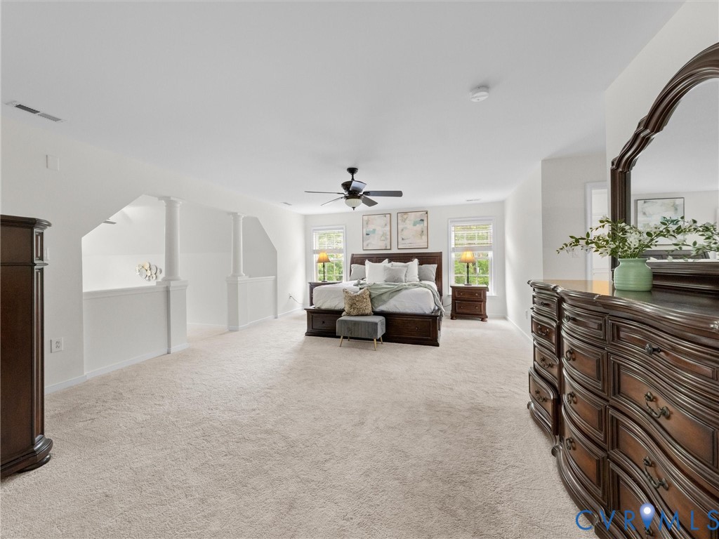 Expansive carpeted room featuring a ceiling fan, multiple windows, and a partial wall with decorative columns