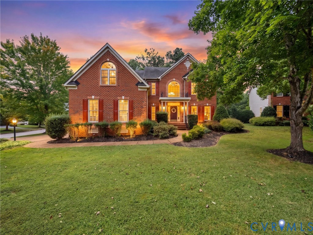 Brick facade residence featuring a covered entry, arched window elements, mature landscaping, and an expansive lawn Brick facade residence featuring a covered entry, arched window elements, mature landscaping, and an expansive lawn