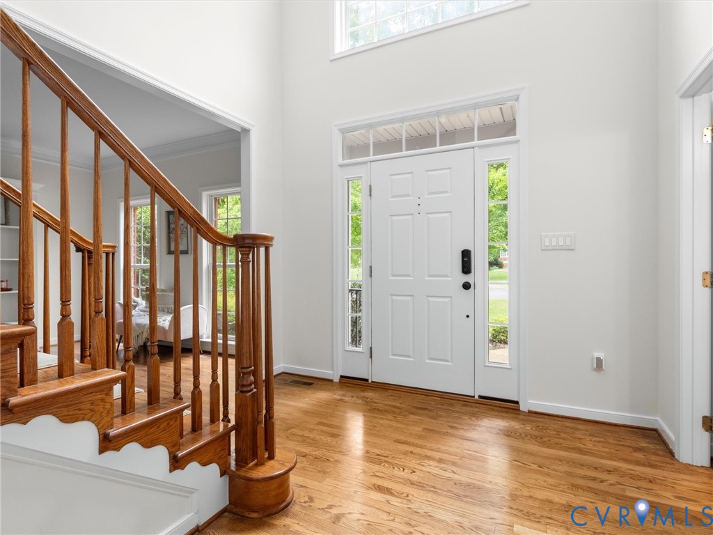 Two-story foyer featuring hardwood flooring, a white paneled front door with sidelights and transom windows, and a hardwood staircase with a decorative newel post