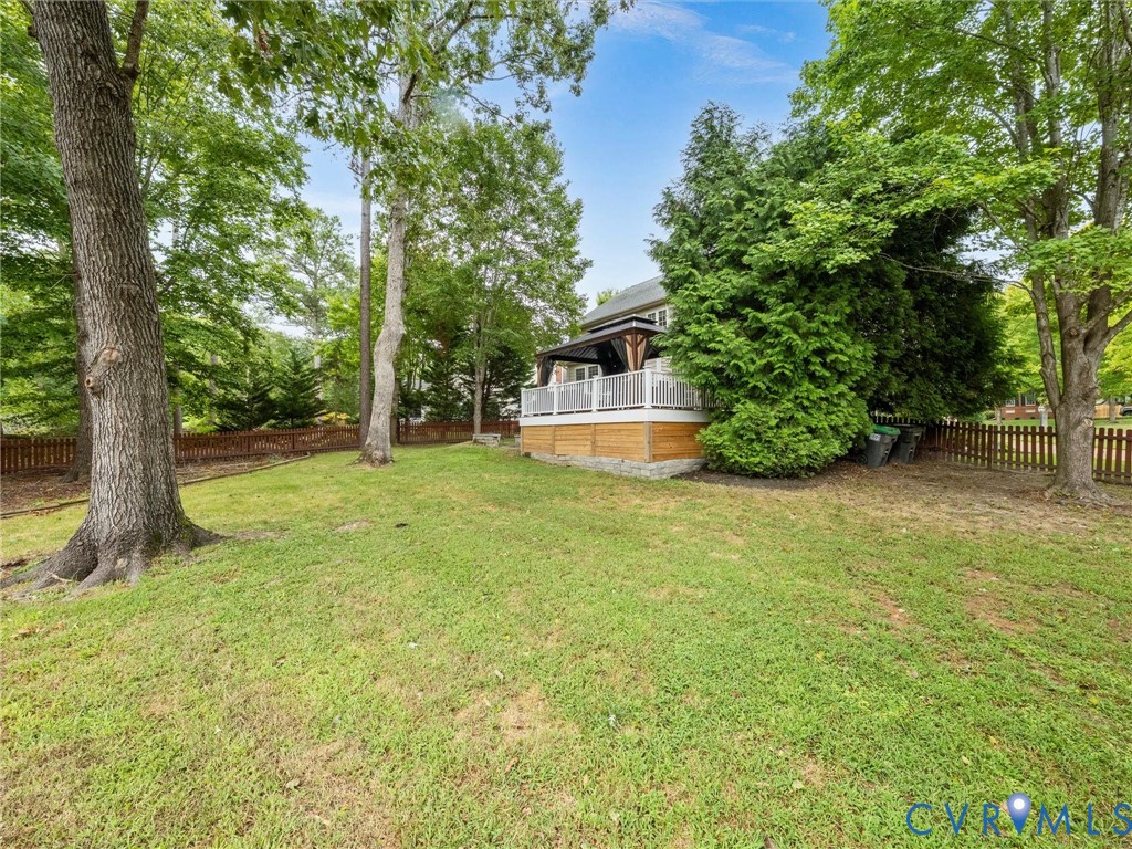 Expansive grassy yard with mature trees, a wood-slat privacy fence, and a raised exterior deck featuring white railings