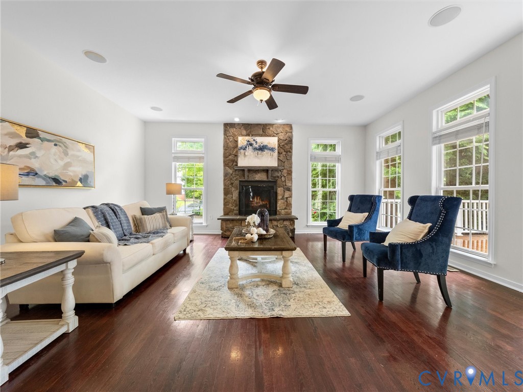 Hardwood flooring, stone-clad fireplace, recessed lighting, ceiling fan, and multiple windows