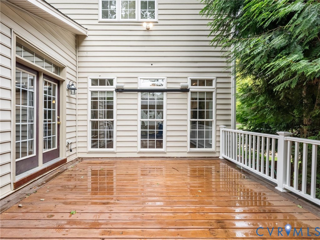 Expansive wood deck with white railing, multiple windows, double glass doors, and cream-colored siding