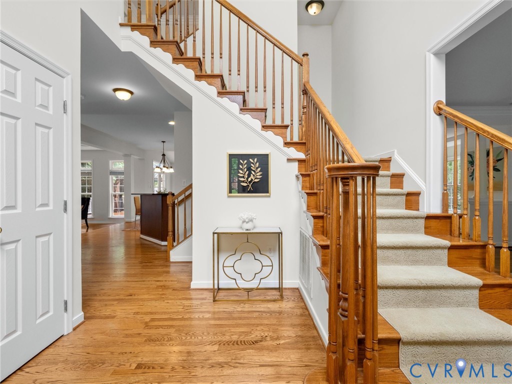 Hardwood flooring, white paneled door, wood staircase with carpet treads, wood banister with spindles, recessed lighting