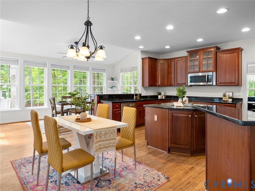 Kitchen and dining area featuring wood-finish flooring, dark wood cabinetry, recessed lighting, and a kitchen island with a dark countertop