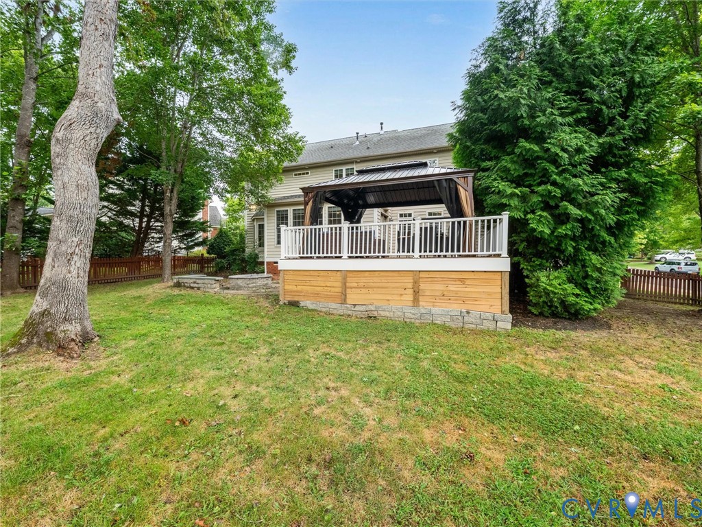 Expansive lawn with mature trees, wooden privacy fence, multi-level composite deck, white railing, and a built-in gazebo with a metal roof
