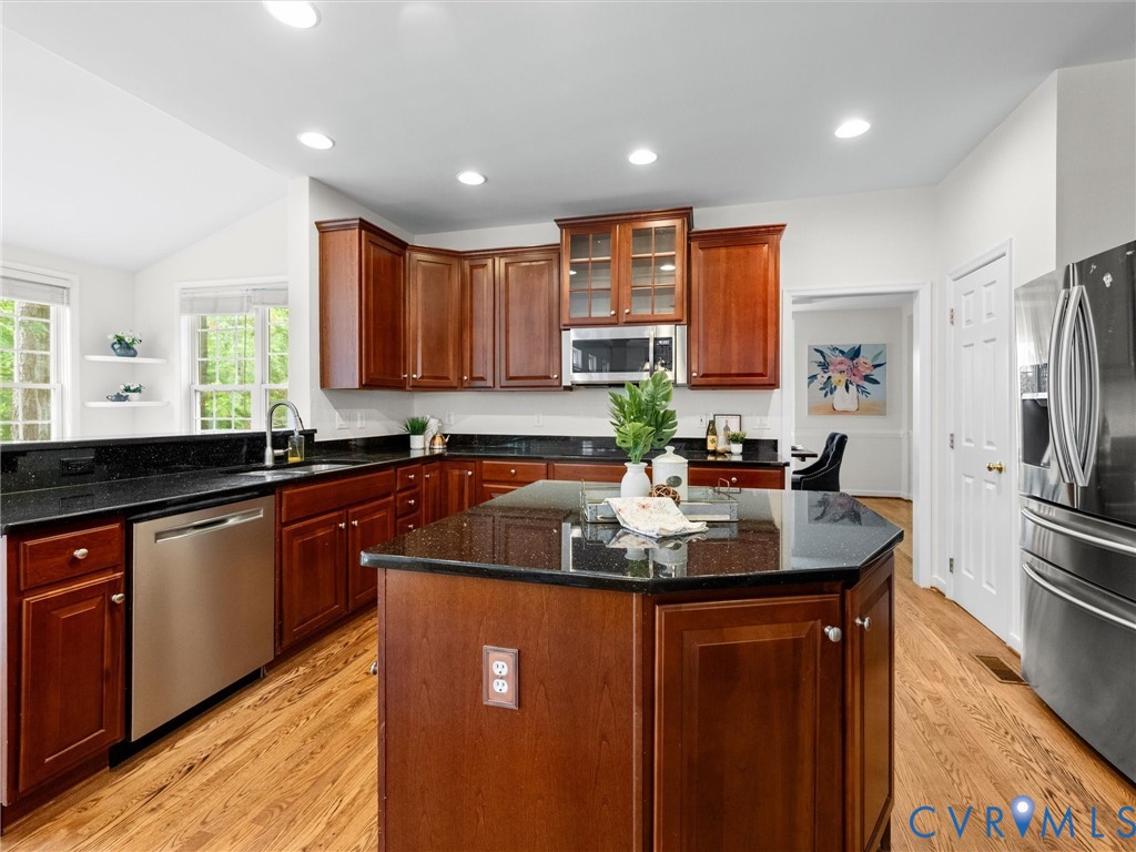 Kitchen featuring an angled island, rich wood cabinetry, dark countertops, stainless steel appliances, and wood-finish flooring
