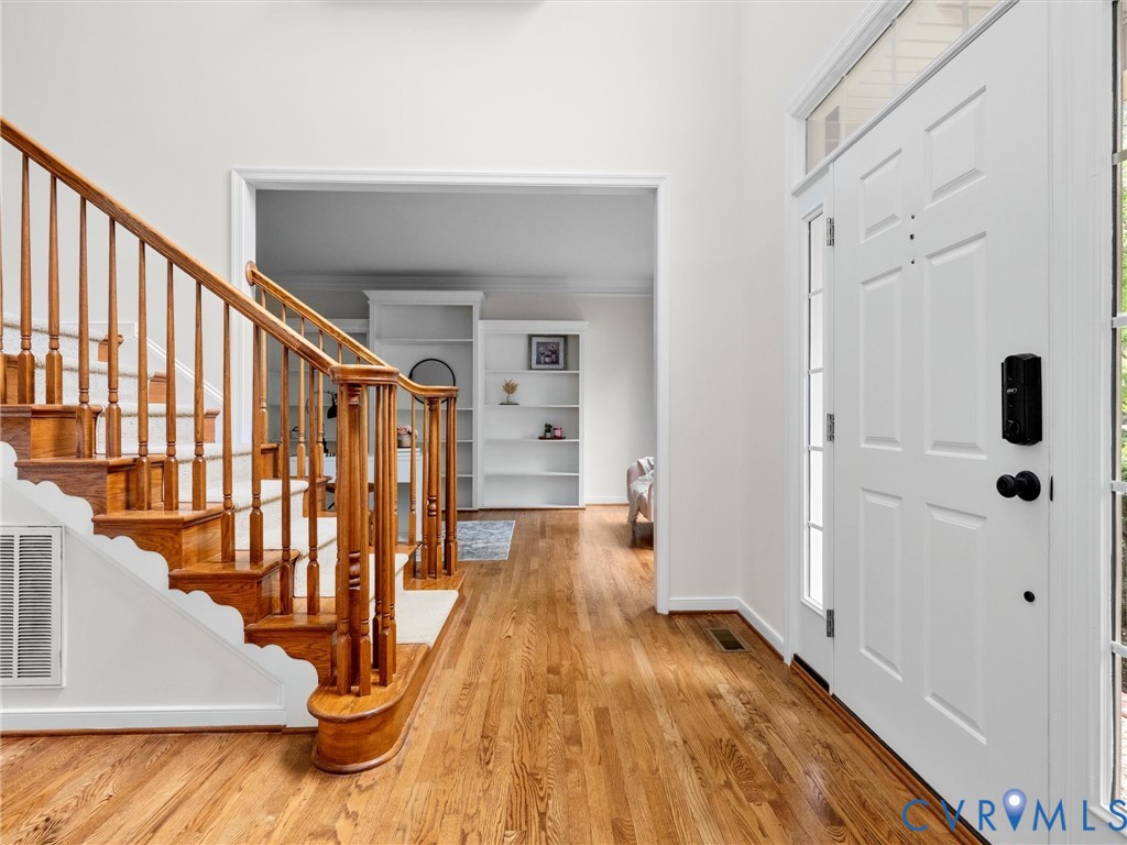 Hardwood flooring throughout the entry, staircase with wood banister and white risers, white paneled entry door with sidelights, and transoms