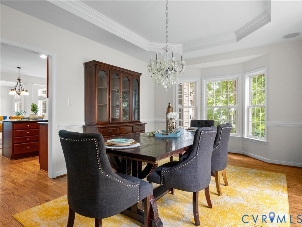 Hardwood flooring, bay window with multiple panes, crown molding, chair rail, and an ornate crystal chandelier