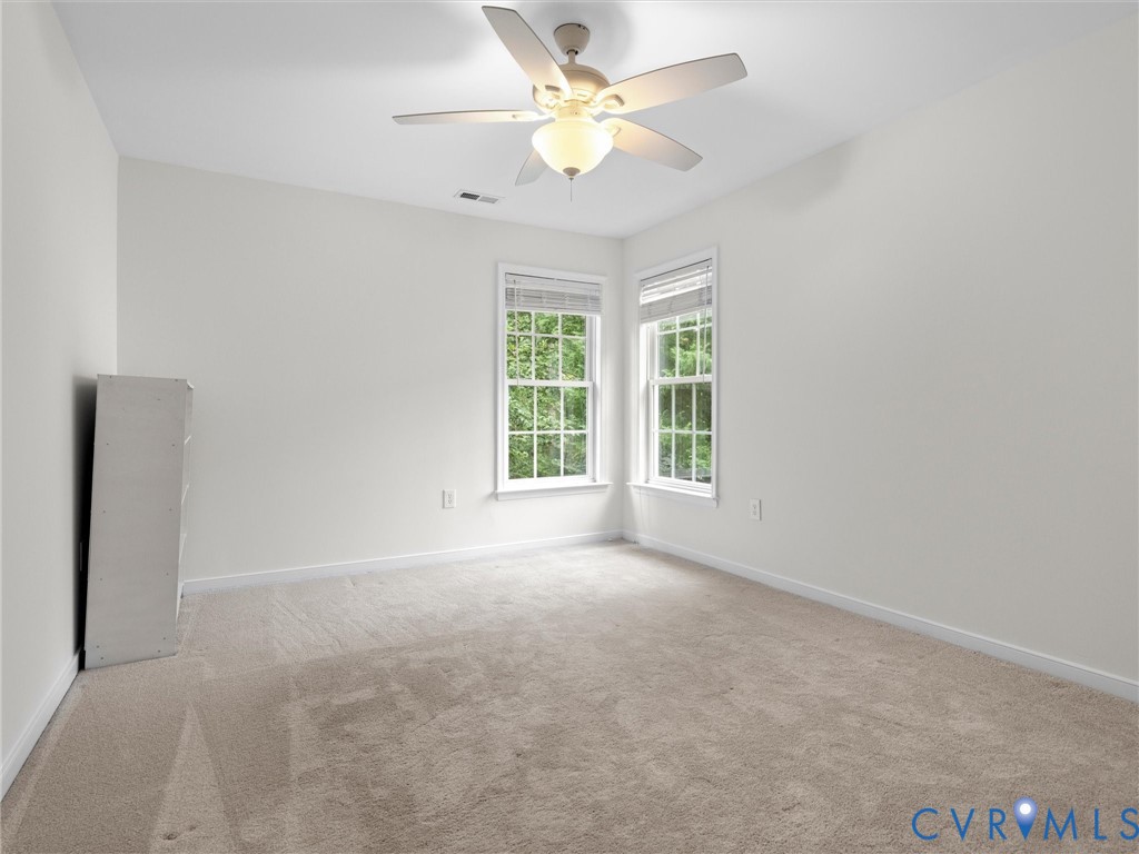 Angled ceiling, dual windows with blinds, ceiling fan with integrated lighting, and neutral carpeting