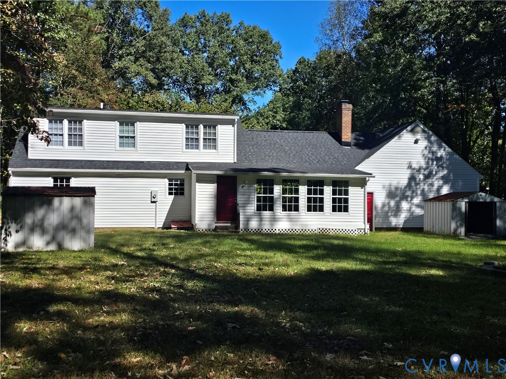Exterior siding featuring white horizontal lap, a dark asphalt shingle roof, a brick chimney, and grid-pattern window panes, set on a wooded lot Exterior siding featuring white horizontal lap, a dark asphalt shingle roof, a brick chimney, and grid-pattern window panes, set on a wooded lot