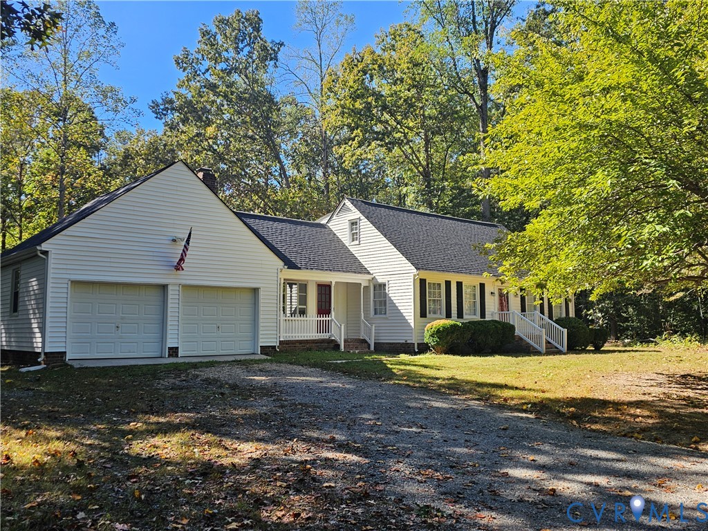 Cape Cod-style residence featuring white siding, dark shutters, a two-car garage, and white railed porch entries, situated on a wooded lot