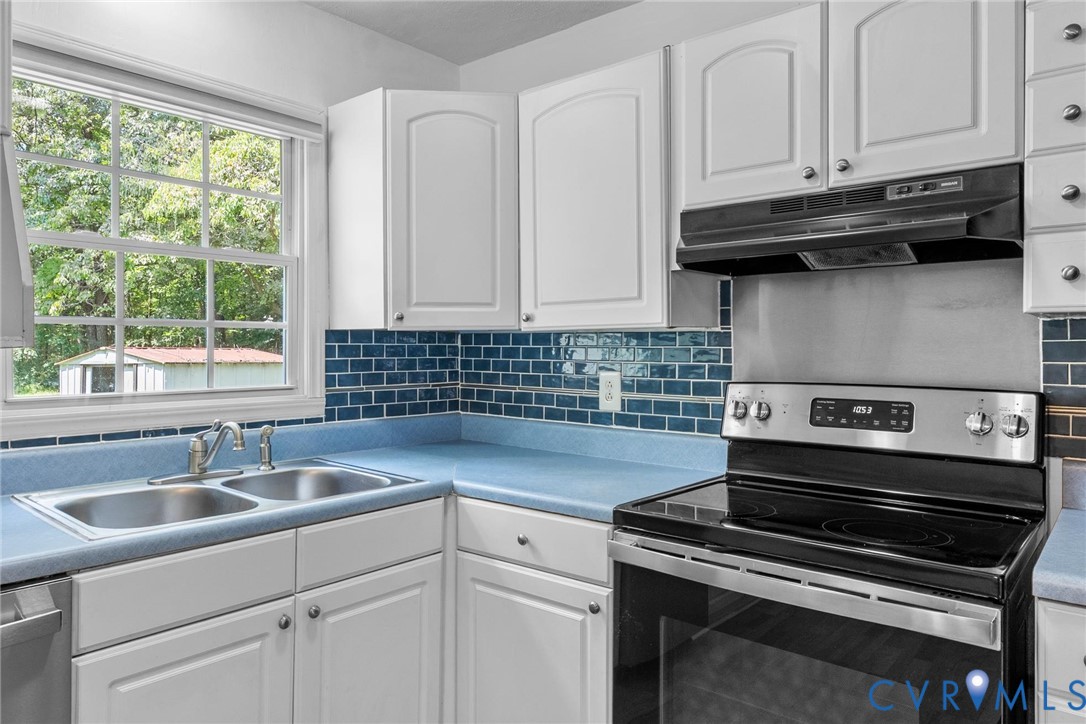 White cabinetry with brushed nickel hardware, blue subway tile backsplash, stainless steel electric range, and double basin stainless steel sink