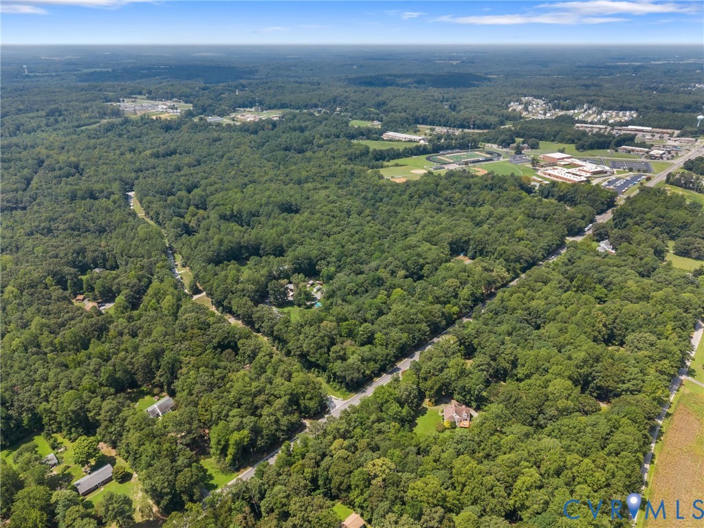 Expansive wooded property featuring a residential structure, surrounding roadways, and distant commercial structures Expansive wooded property featuring a residential structure, surrounding roadways, and distant commercial structures
