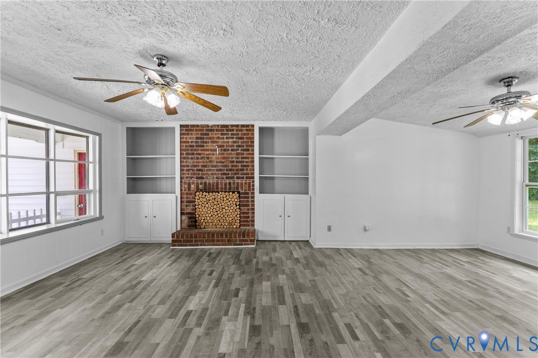Wood-finish flooring, brick fireplace with hearth, built-in shelving, built-in cabinetry, and ceiling fans