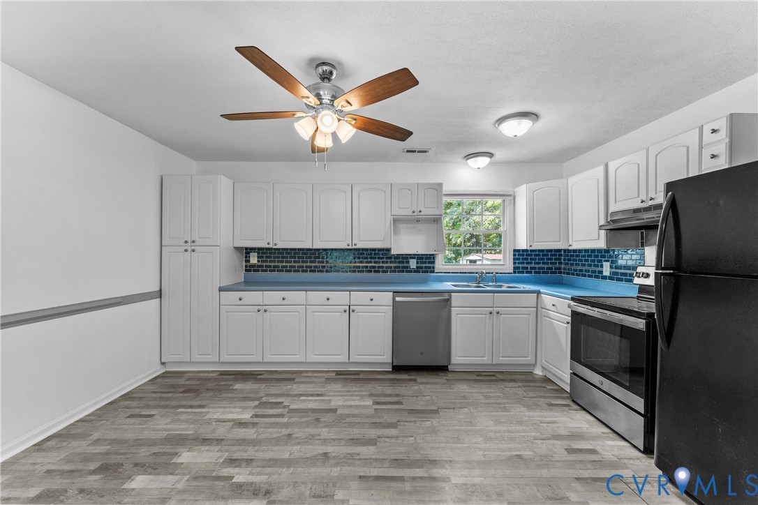 Kitchen featuring white cabinetry, blue countertops, a blue subway tile backsplash, stainless steel appliances, and wood-finish flooring Kitchen featuring white cabinetry, blue countertops, a blue subway tile backsplash, stainless steel appliances, and wood-finish flooring