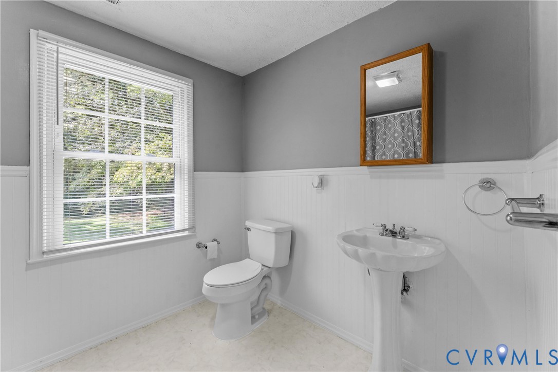 White pedestal sink with chrome faucet, toilet, and a window with horizontal blinds