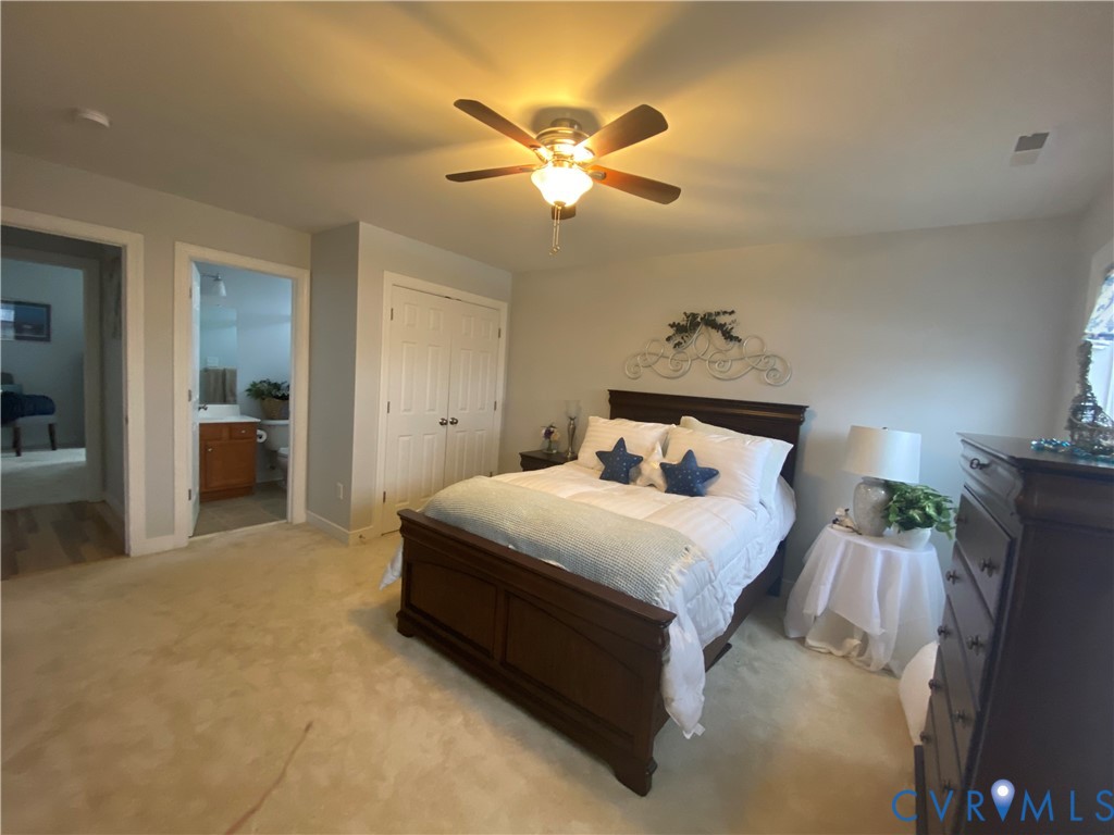 Carpeted bedroom featuring a ceiling fan with integrated lighting, double bi-fold closet doors, and access to a full bathroom with a wood-finish vanity