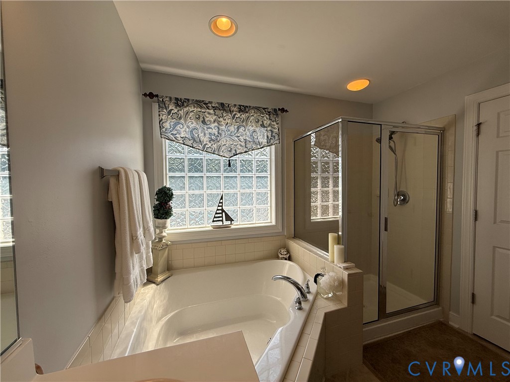Soaking tub with tile surround, glass block window, and adjacent glass-enclosed shower