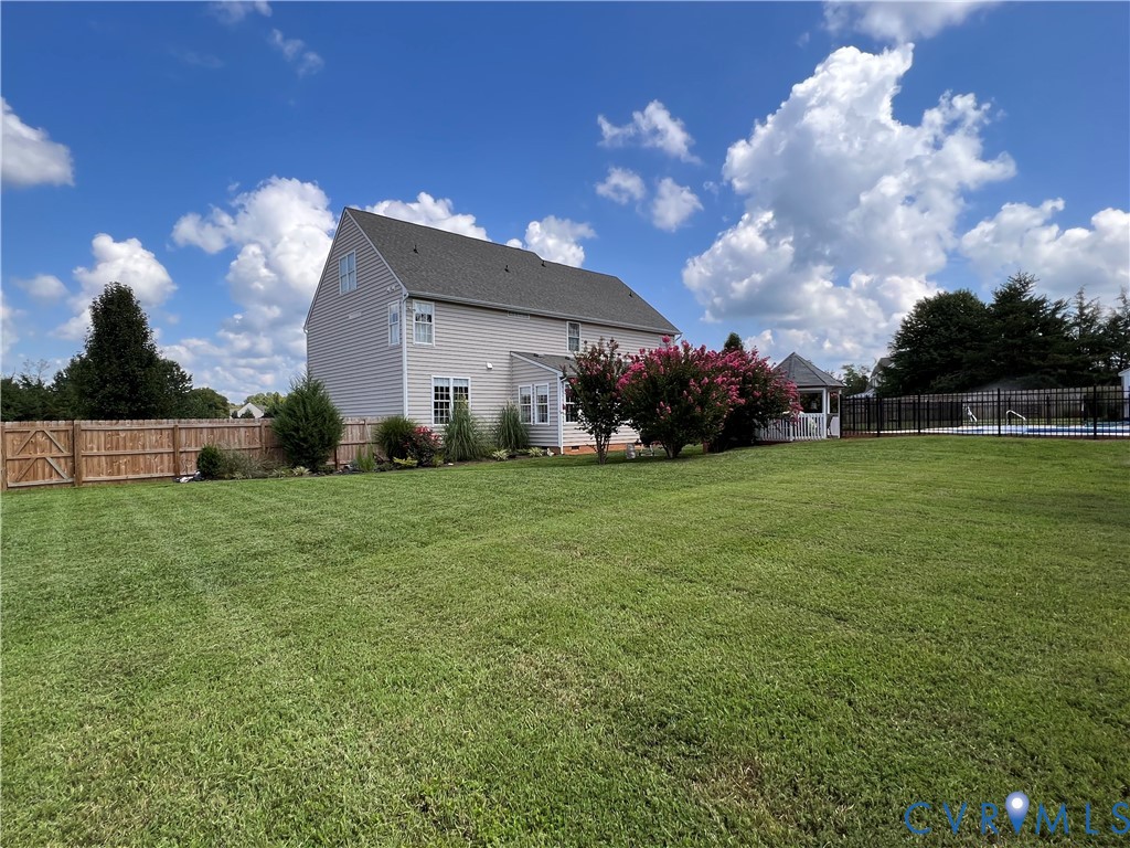 Spacious backyard featuring a large green lawn, wood privacy fencing, and mature landscaping