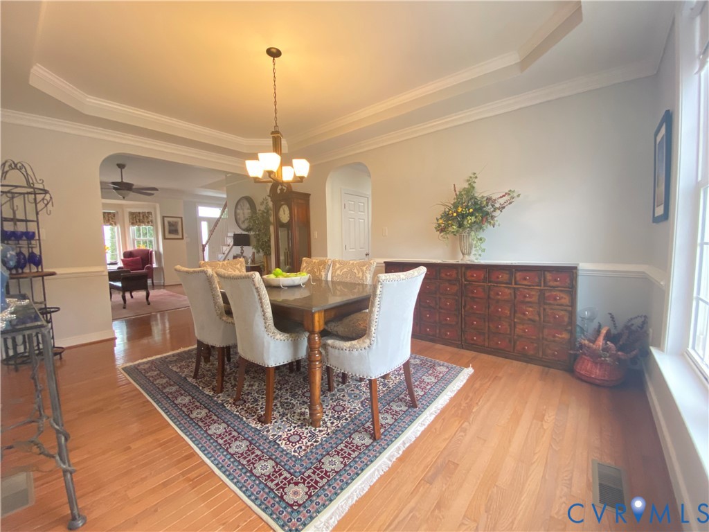 Dining area featuring hardwood flooring, tray ceiling with crown molding, wainscoting, and an arched entryway
