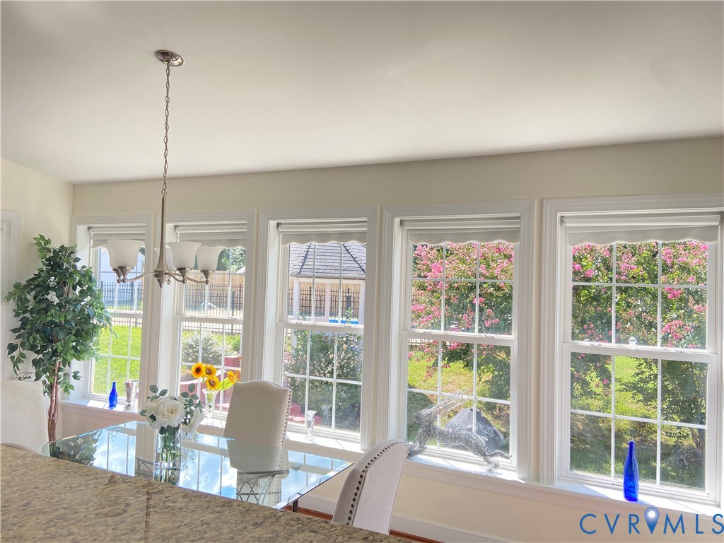Dining area featuring a contemporary chandelier, multiple large windows with white trim, and a clear glass-top dining table