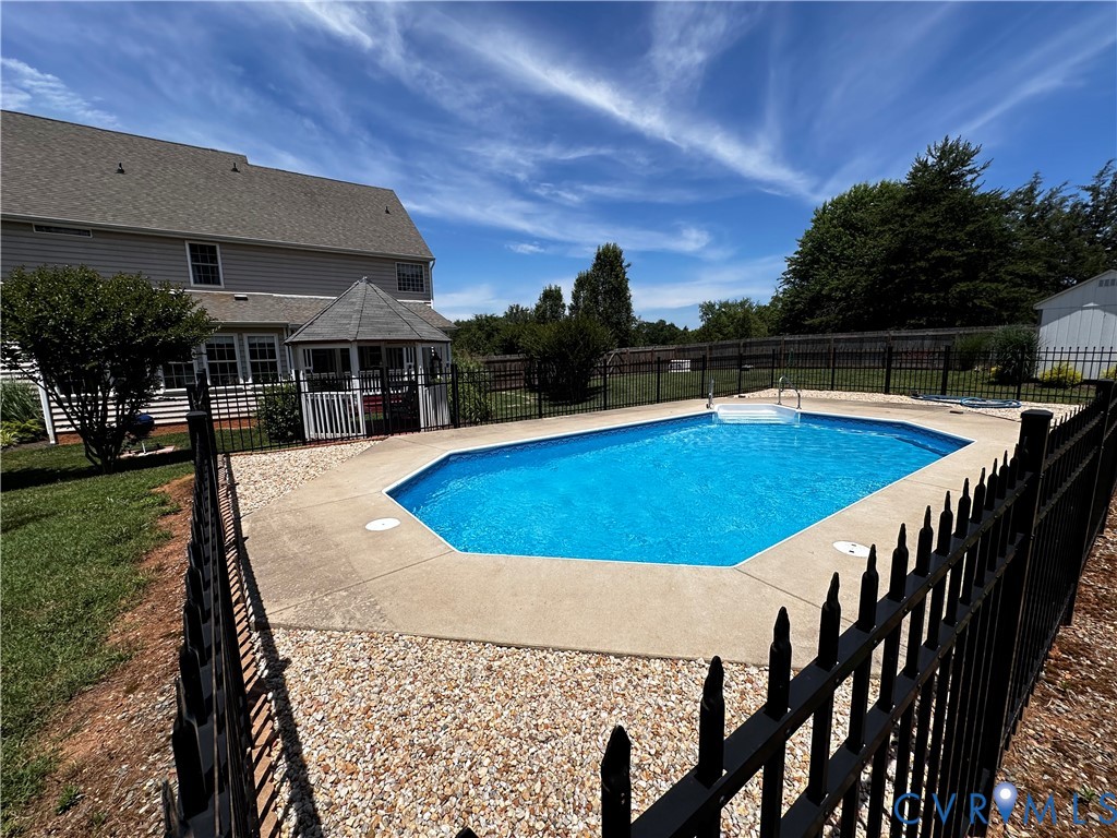 Fenced backyard featuring an in-ground swimming pool with concrete surround and a nearby gazebo structure