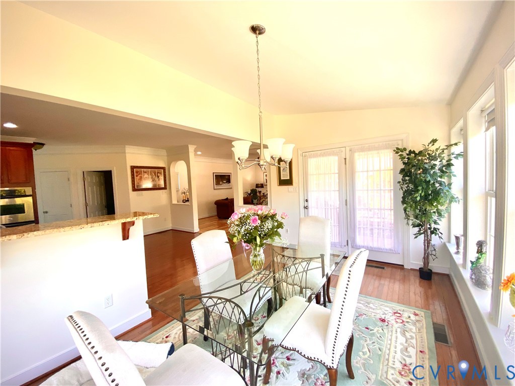 Dining area featuring hardwood flooring, a multi-light chandelier, and abundant natural light from multiple windows and French doors