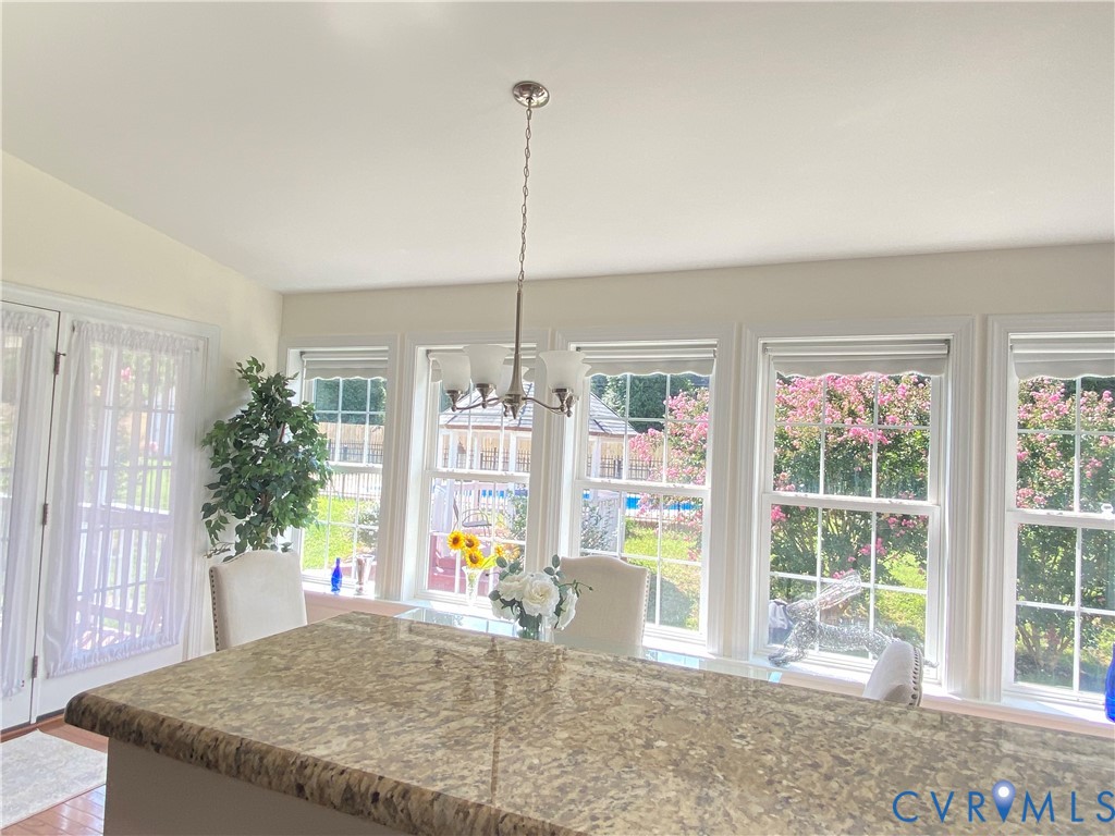 Bright interior space featuring a large granite-look island, multiple windows with white trim, and a brushed nickel chandelier