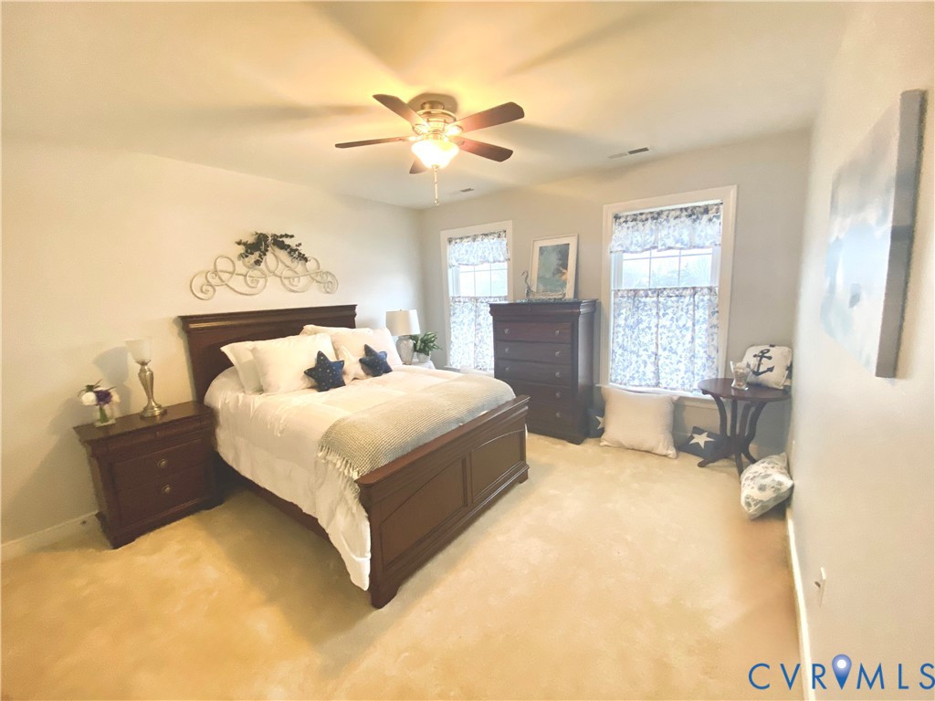 Carpeted interior space featuring light-toned walls, two windows, and a ceiling fan with integrated lighting