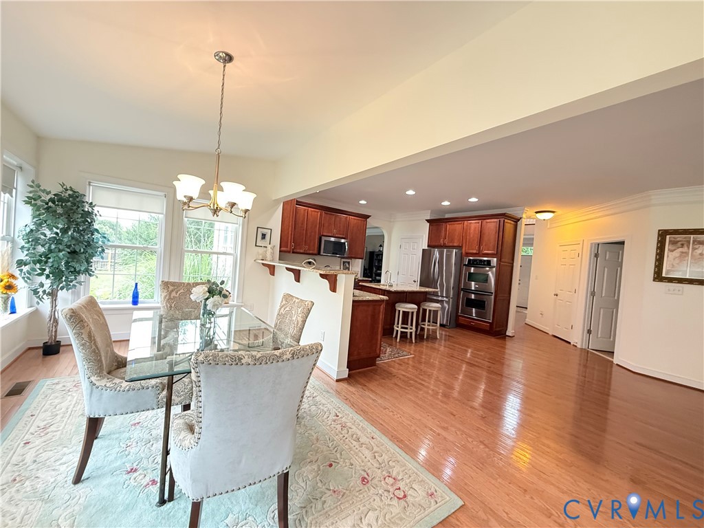 Open-concept dining area featuring wood-finish flooring, a contemporary chandelier, and a breakfast bar Open-concept dining area featuring wood-finish flooring, a contemporary chandelier, and a breakfast bar