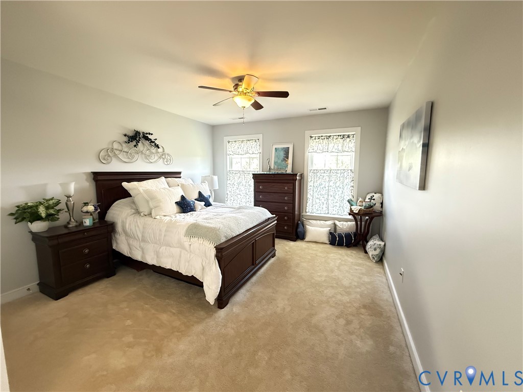 Carpeted room featuring a ceiling fan with integrated lighting, two windows with white trim, and light-colored walls