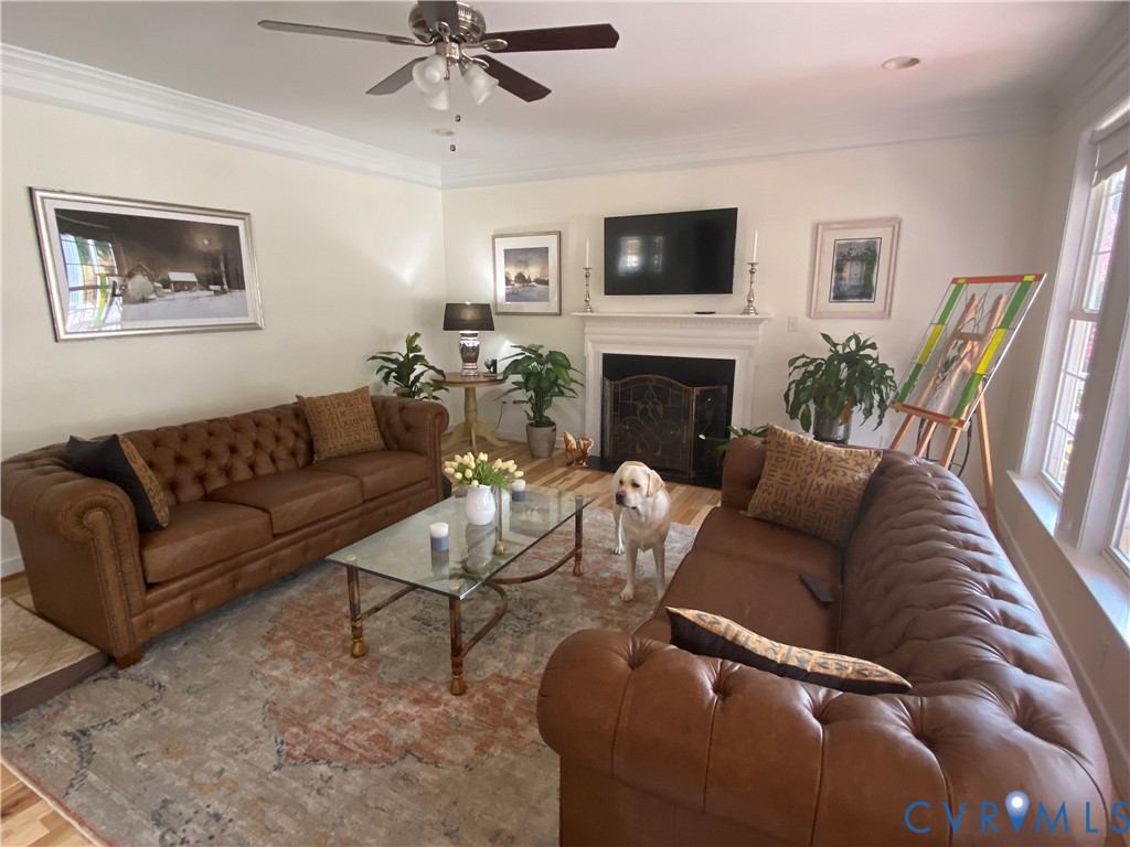 Spacious living area featuring a central fireplace with an ornate screen, crown molding, wood-finish flooring, and multiple windows