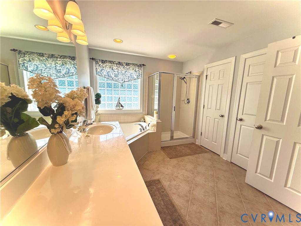 Bathroom featuring a dual vanity with integrated sinks, a corner garden tub, a glass-enclosed shower, recessed lighting, and tile flooring