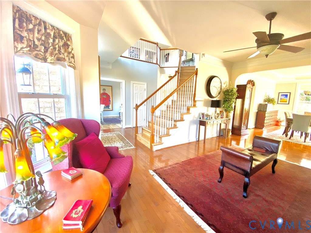 Hardwood flooring extending throughout the main level, staircase with white spindles and wood handrail, and an arched entryway