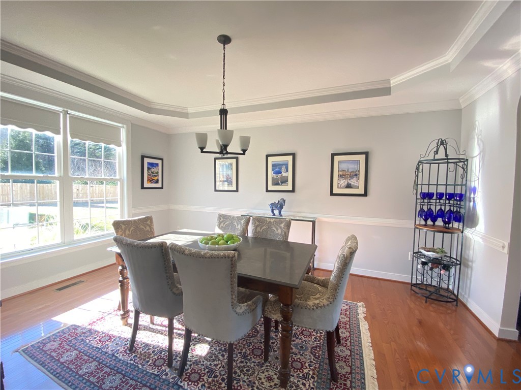 Dining area featuring wood-finish flooring, a tray ceiling with crown molding, and a chandelier