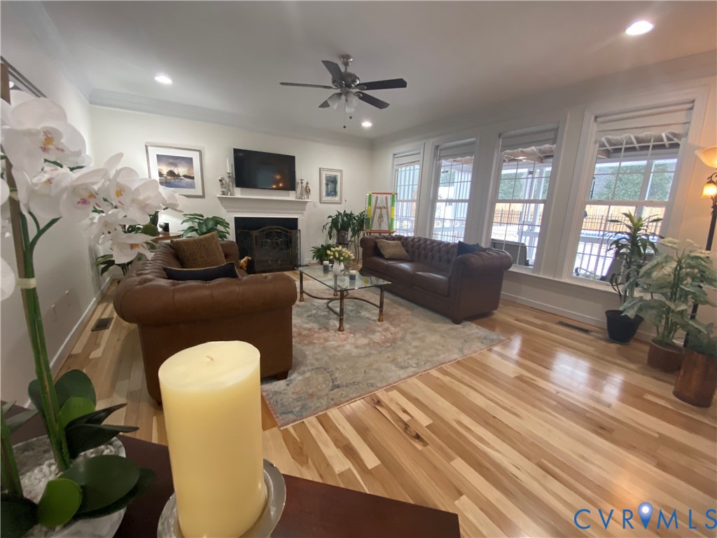 Spacious living area featuring light wood-finish flooring, a traditional fireplace with a white mantel, recessed lighting, and a ceiling fan