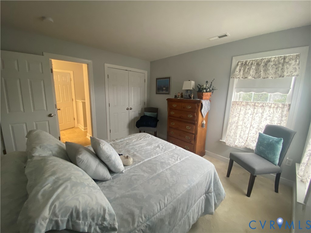 Bedroom featuring light gray walls, plush carpet flooring, a window with decorative valances, and a double-door closet