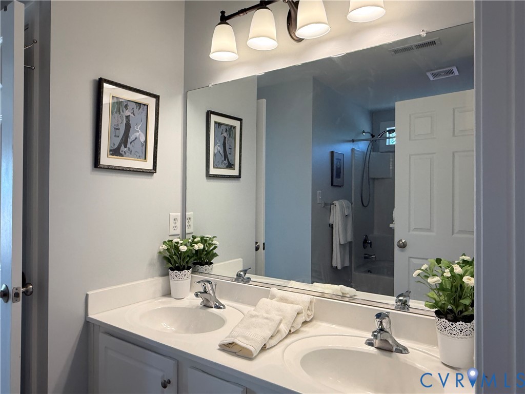 Dual vanity with integrated sinks, white cabinetry, chrome fixtures, and a large wall-mounted mirror