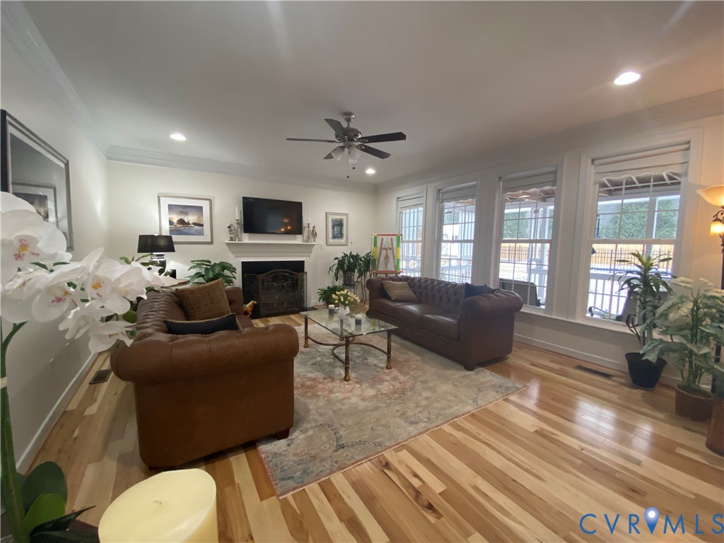 Spacious living area featuring wood-finish flooring, a white mantel fireplace with an ornate screen, and triple windows providing natural light