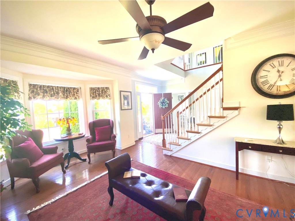 Foyer featuring hardwood flooring, a multi-paneled front door, a staircase with white balusters and wood handrails, a bay window, and a ceiling fan